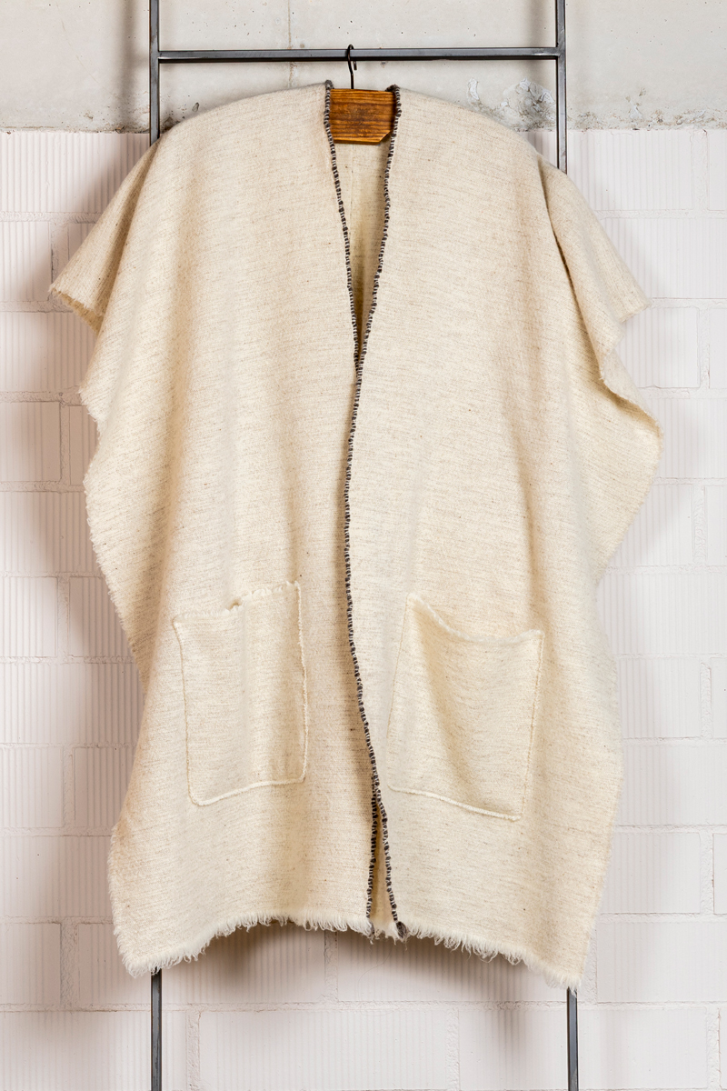 Poncho SALP lana merina tono crudo y perfil marron tejido en telar manual en Barcelona. A poncho in 100% merino wool handwoven in Barcelona in off white color and brown artisanal edges