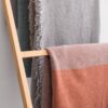 Mantas de lana merina y yak en colores gris, cobre y turquesa colgadas sobre expositor de madera