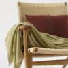 Manta lana cashmere en color oliva con perfil turquesa apoyada sobre silla