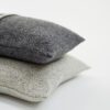 Cojines de diseño de lana merina apilados en negro y gris claro. Foto de estudio de cojines sobre fondo blanco
