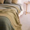Cojín y manta de lana merino con trazabilidad diseño en cuadrados verdosos, amarillos y azules con perfiles en amarillo expuestos sobre cama