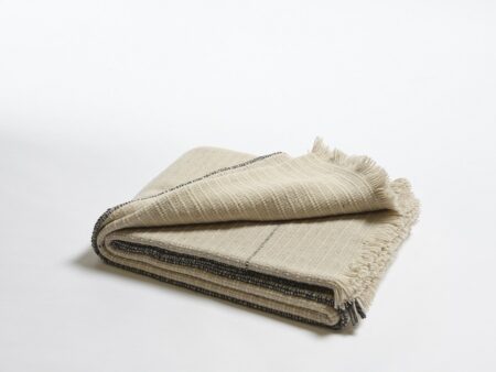 Manta de lana merino tejida en telar manual con trazabilidad en colores neutros con perfiles internos en gris doblada 