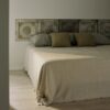 Manta de diseño de Teixidors Nebula en lana cashmere y merina en tono crudo cubriendo una cama. Cojines de diseño en lana cashmere en tonos oliva