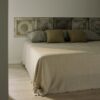 Manta de diseño de Teixidors Nebula en lana cashmere y merina en tono crudo cubriendo una cama. Cojines de diseño en lana cashmere en tonos oliva