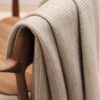 Manta de diseño realizada por John Pawson para Teixidors de lana merino en color mármol. Manta de diseño con franjas rectangulares apoyada sobre silla Carl Hanssen en madera