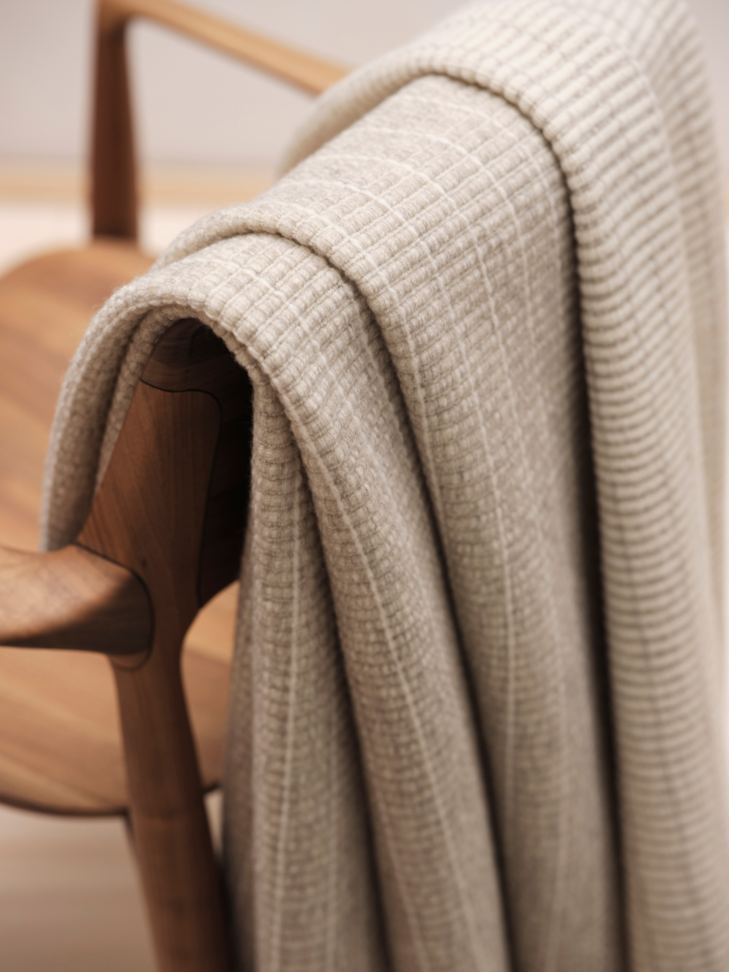 Manta de diseño realizada por John Pawson para Teixidors de lana merino en color mármol. Manta de diseño con franjas rectangulares apoyada sobre silla Carl Hanssen en madera