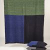 Manta de lana merino tricolor en colores azul verde, marino y negro expuesta sobre soporte de madera horizontal