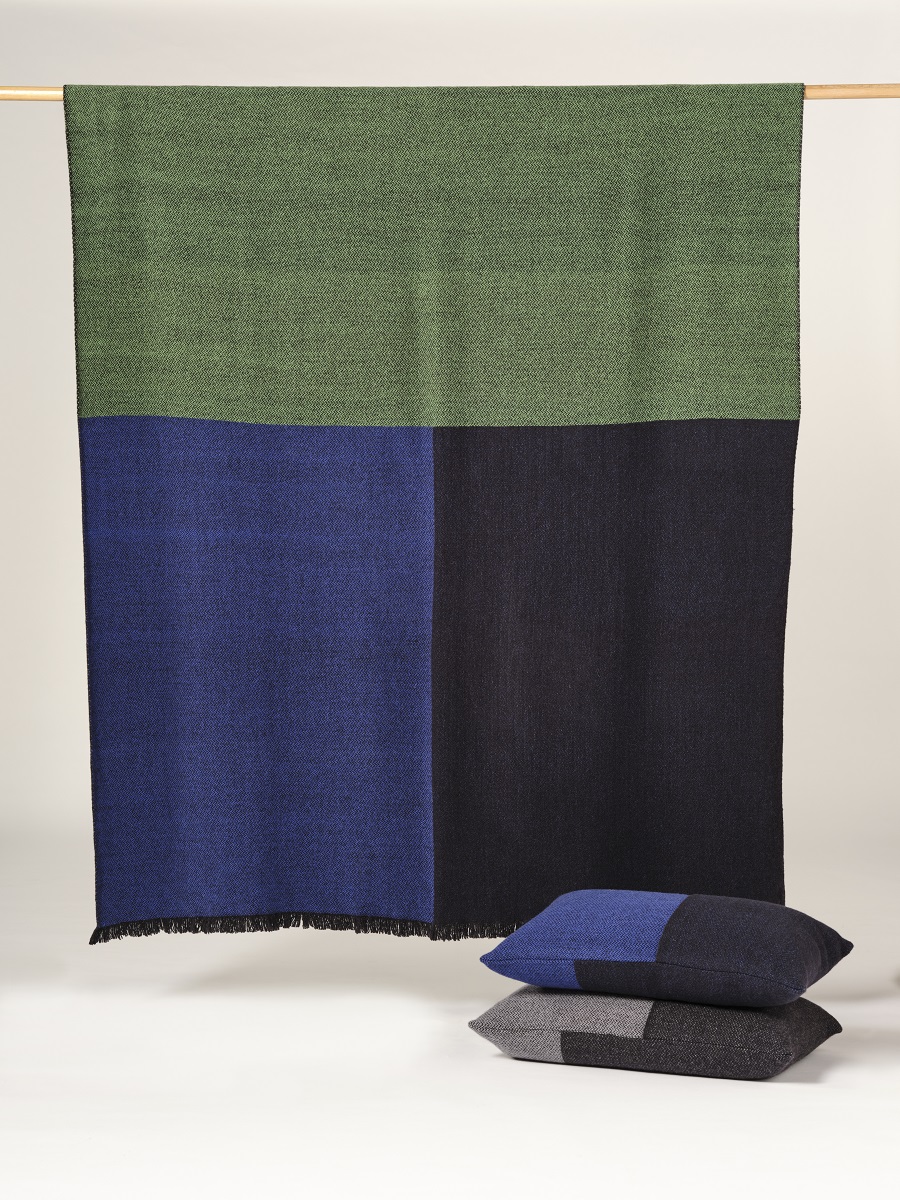 Manta de lana merino tricolor en colores azul verde, marino y negro expuesta sobre soporte de madera horizontal 