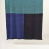 Manta de lana merino en colores azul turquesa, marino y negro expuesta sobre soporte de madera horizontal
