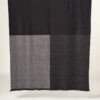 Manta de lana merino tricolor en colores negro, gris marengo, gris oscuro expuesta sobre soporte de madera horizontal