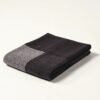 Manta de diseño Teixidors doblada en lana merino en color gris y negro. Foto de estudio sobre fondo blanco
