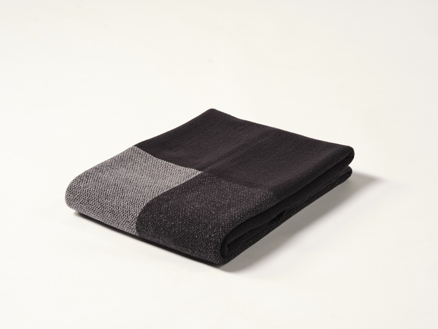 Manta de diseño Teixidors doblada en lana merino en color gris y negro. Foto de estudio sobre fondo blanco
