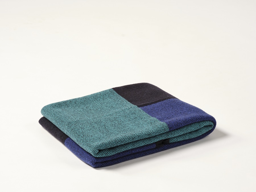 Manta de diseño Teixidors doblada en lana merino en color azul turquesa, azul marino y negro. Foto de estudio sobre fondo blanco
