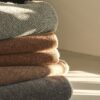 Cinco mantas de diseño en lana merino apilados. En tonos anaranjados, verde y gris