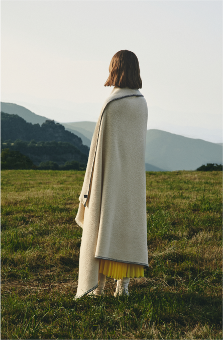 Persona en una pradera cubriendose con una manta teixidors de diseño en lana merina color blanca