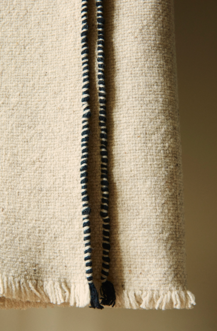 Manta de diseño Teixidors en lana merina en tono natural con perfil manual en color negro