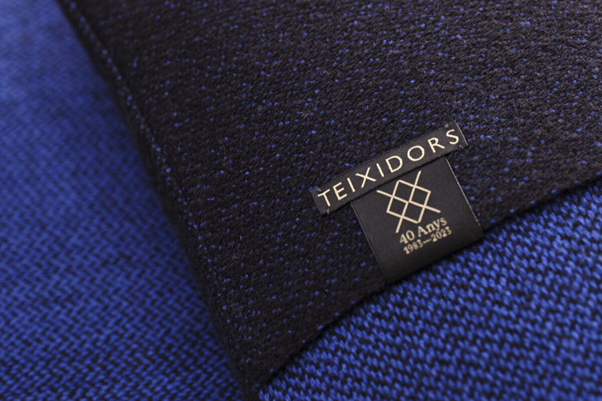 Cojin de diseño en lana merino color azul marino y azul oscuro. Etiquetado con el logo del 40º aniversario de Teixidors
