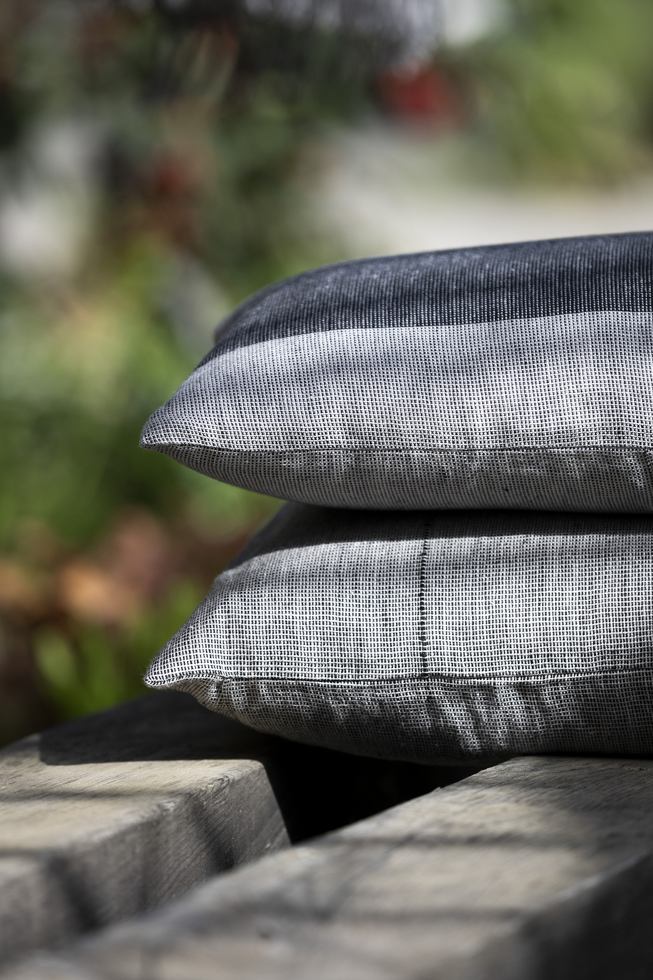 Manta y cojines de lino europeo en tonos grises sobre roca 