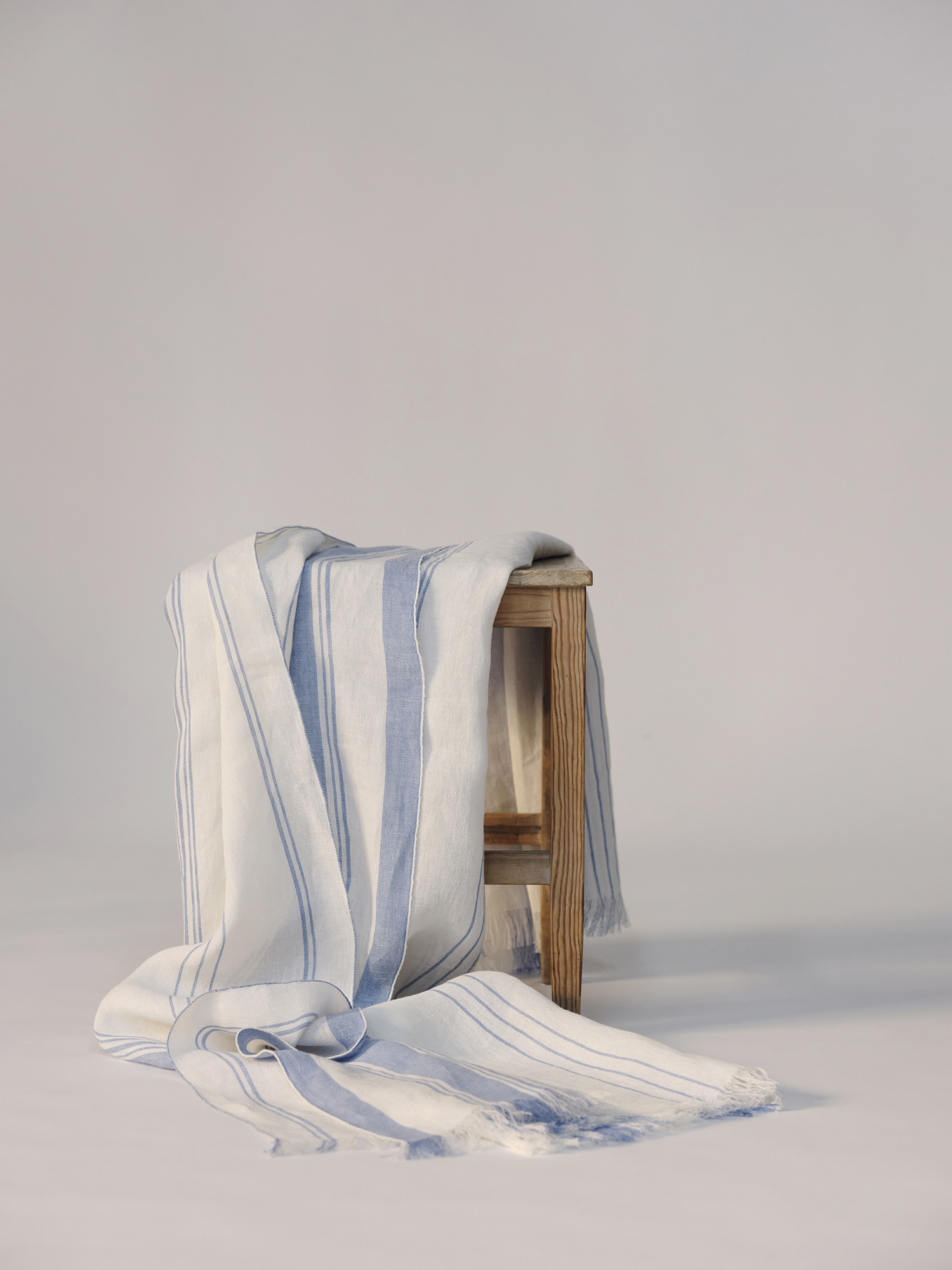 Manta Cama Eunoia de lino europeo con franja azul en extremos sobre silla madera