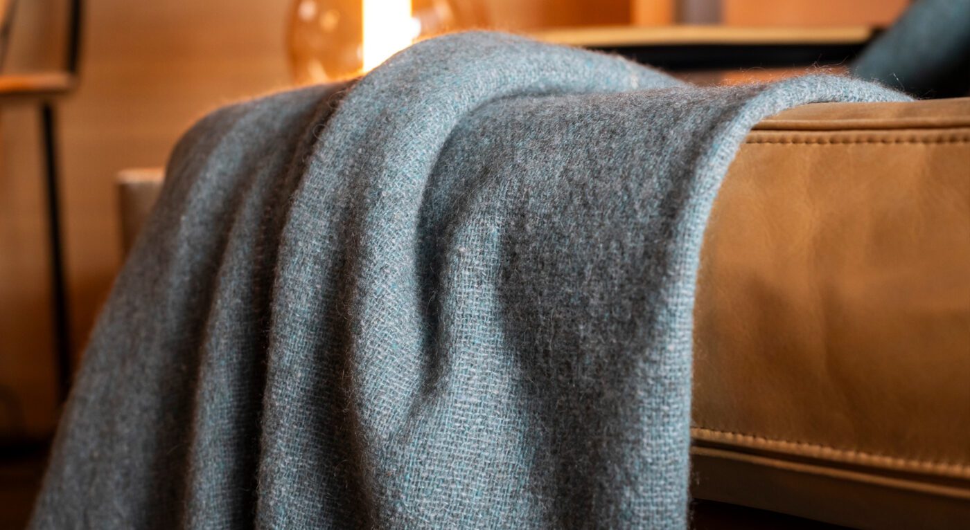 A Nomad throw in grey color, made from merino wool and yak, resting on a sofa
